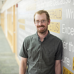 photo of a man with glasses standing next to a wall covered in quoted about writing. 