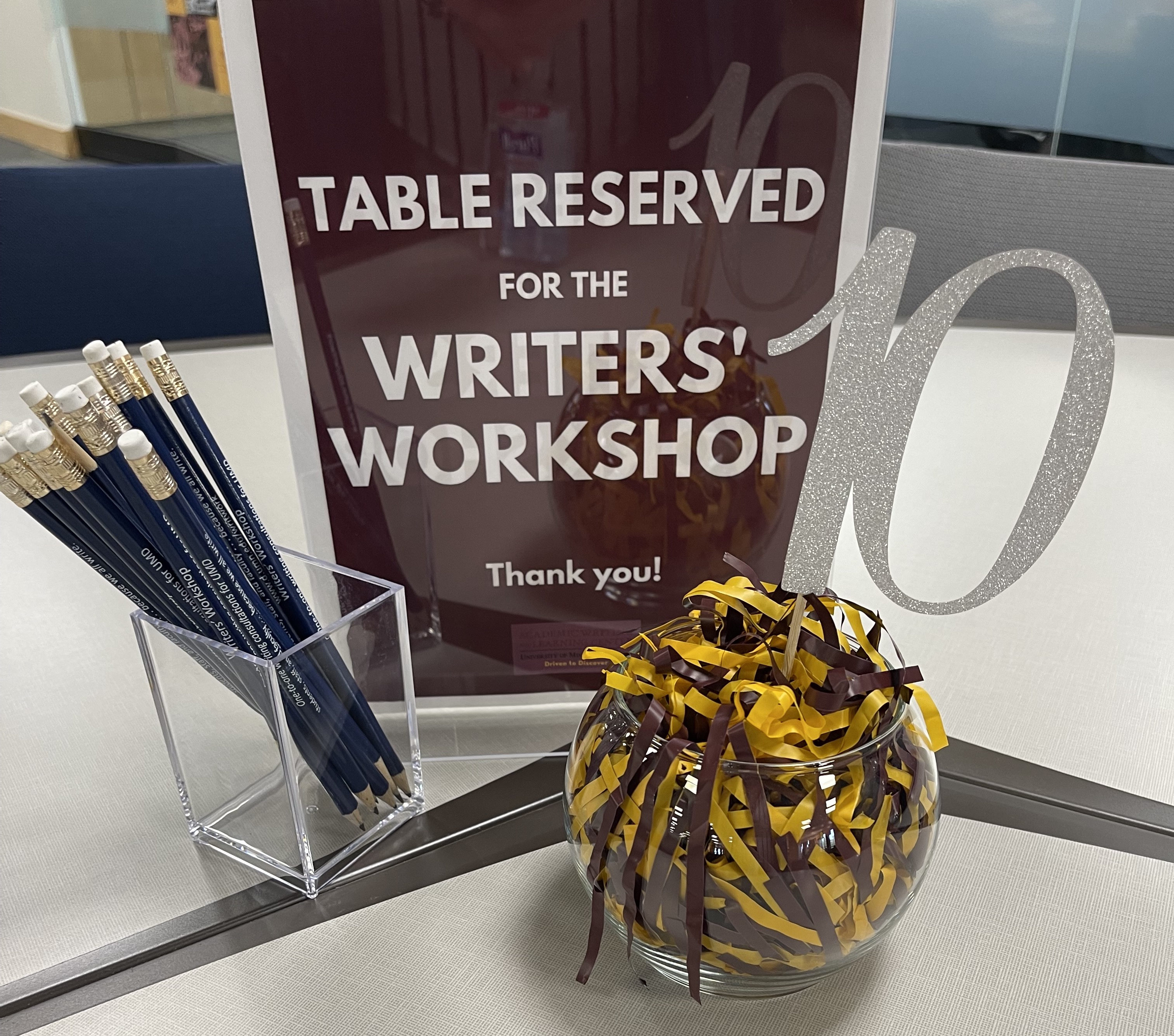 maroon table sign "table reserved for the Writers' Workshop" alongside a cup full of pencils